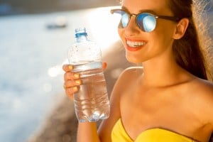 Woman drinking water from transparent bottle on the beach