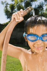 Hispanic boy holding hose over head and wearing goggles