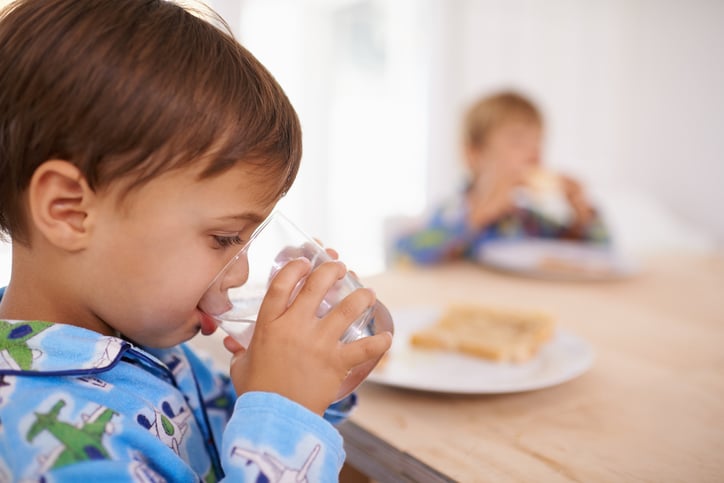 A cute little boy having a drink of water with breakfast