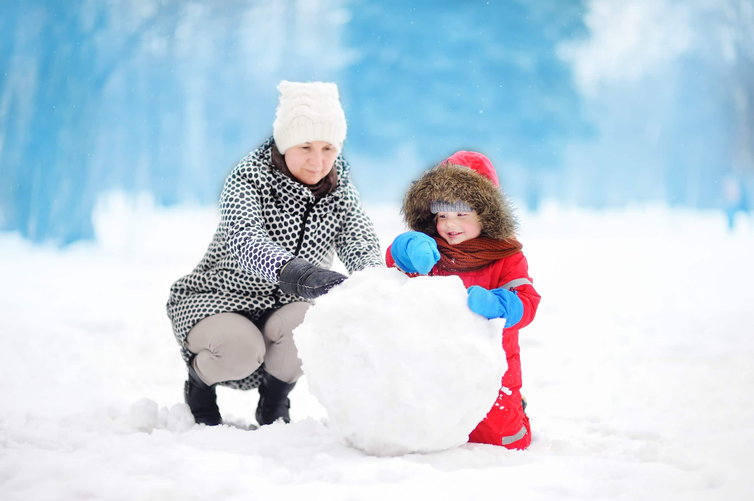Child building a snowman with female adult