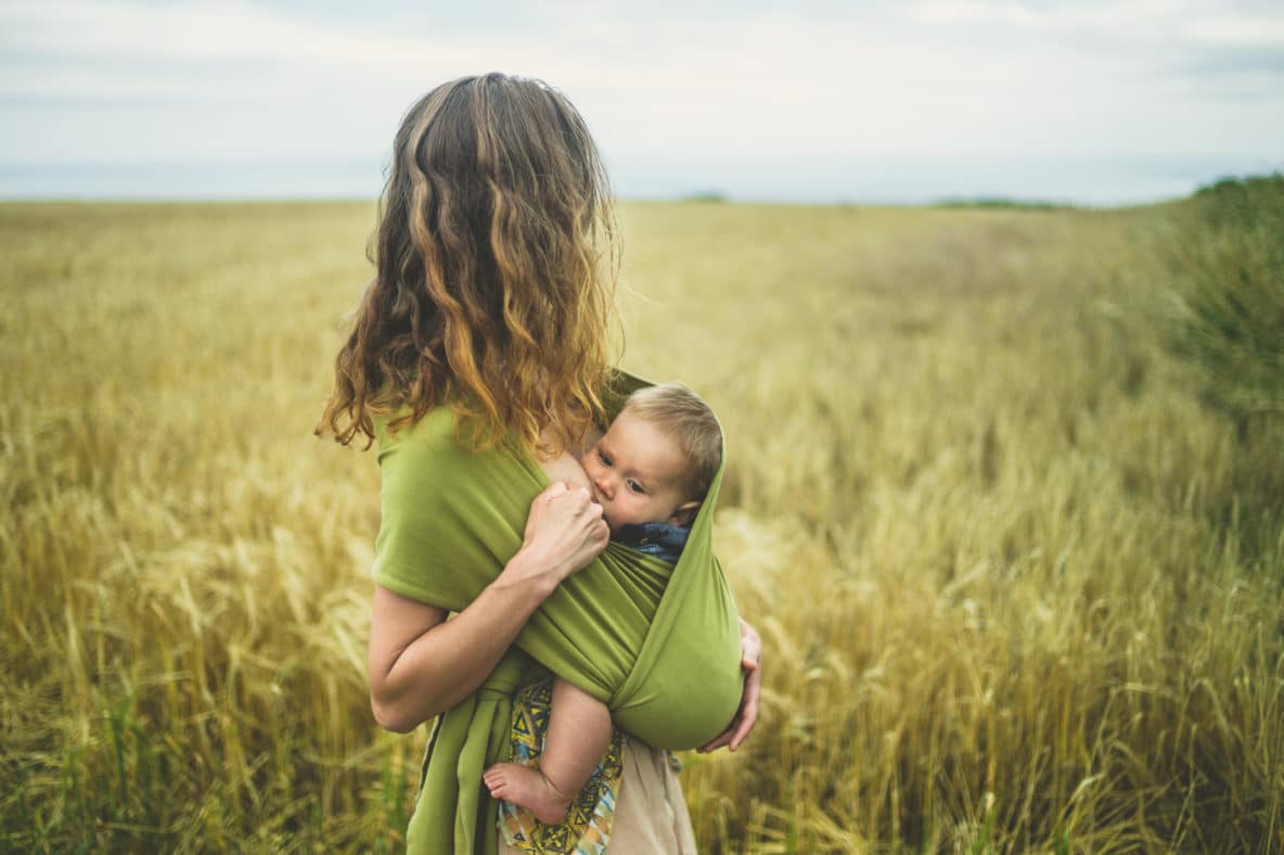 Mother breastfeeding baby in field while baby-wearing