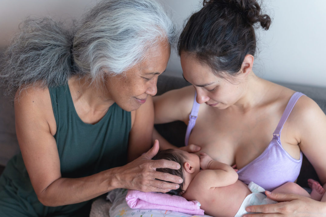 A new young mother gets encouragement from her mom while breastfeeding her infant daughter