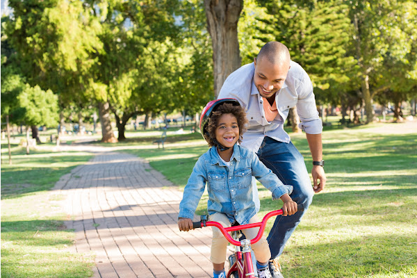 Dad running behind a child helping her to learn to ride her bike.