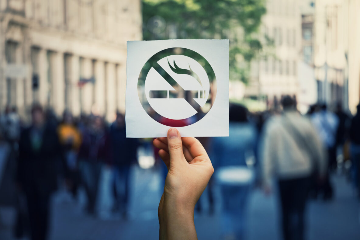 No Smoking symbol raised by a hand in front of a street scene of people walking